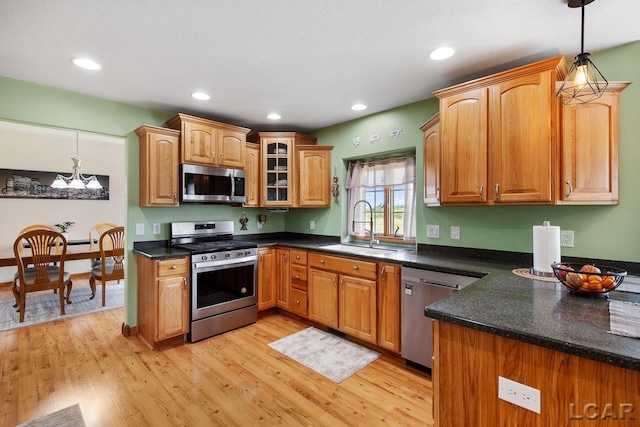 kitchen with appliances with stainless steel finishes, light wood-type flooring, sink, decorative light fixtures, and a chandelier