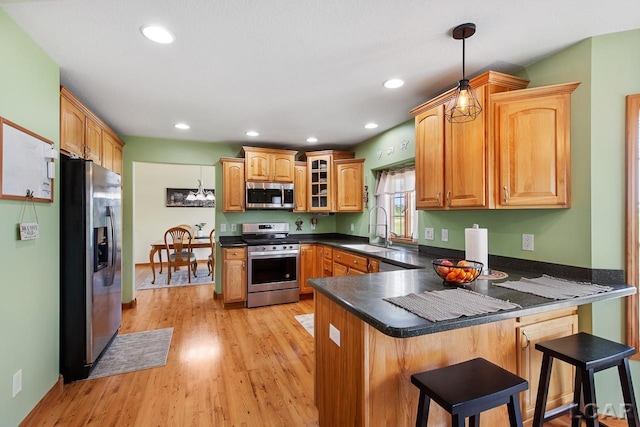 kitchen with kitchen peninsula, appliances with stainless steel finishes, a kitchen breakfast bar, light hardwood / wood-style floors, and hanging light fixtures