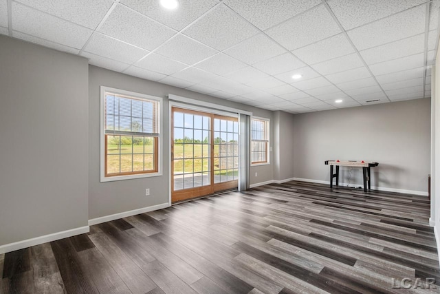 empty room featuring plenty of natural light, a drop ceiling, and dark hardwood / wood-style flooring