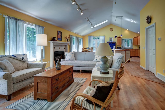 living room with light hardwood / wood-style floors, a tiled fireplace, lofted ceiling with skylight, and track lighting