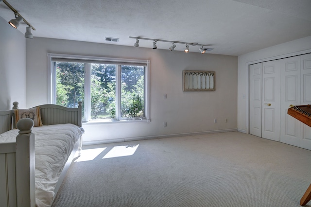 unfurnished bedroom featuring a textured ceiling, rail lighting, light carpet, and a closet