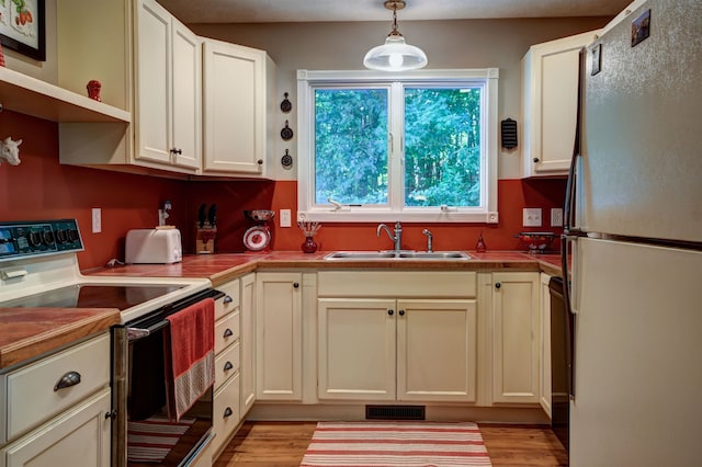 kitchen with sink, white appliances, hanging light fixtures, and light wood-type flooring