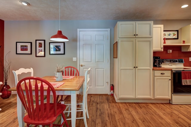 kitchen with white electric range oven, a textured ceiling, decorative light fixtures, and light hardwood / wood-style floors