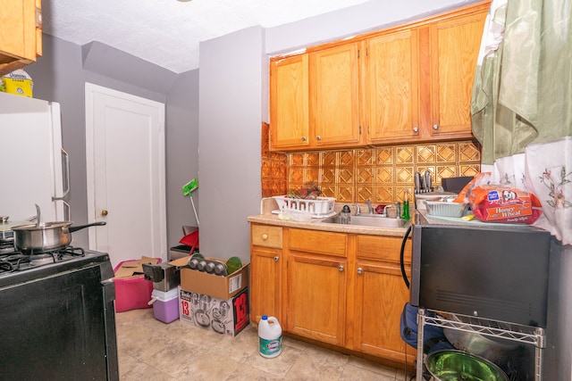 kitchen featuring sink, backsplash, white fridge, black range with gas cooktop, and a textured ceiling