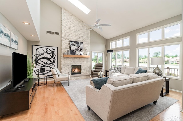 living room featuring light wood-type flooring, a skylight, ceiling fan, high vaulted ceiling, and a fireplace