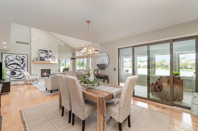 dining room with a stone fireplace, light wood-type flooring, lofted ceiling, and an inviting chandelier