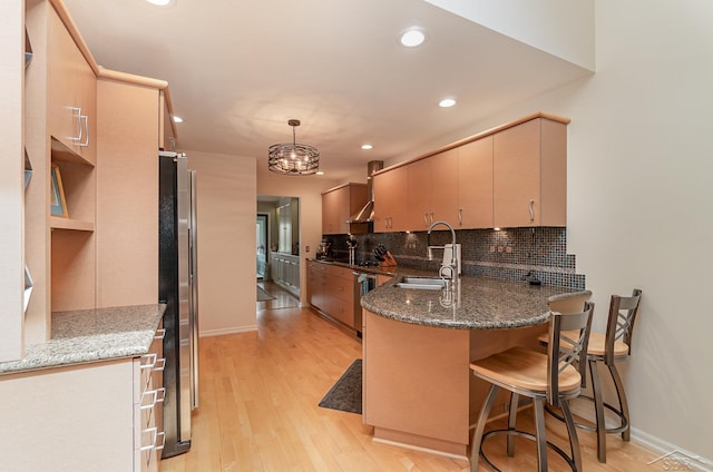 kitchen with pendant lighting, sink, light hardwood / wood-style flooring, kitchen peninsula, and stainless steel refrigerator