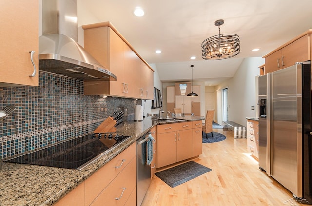 kitchen with light brown cabinets, hanging light fixtures, stainless steel appliances, wall chimney range hood, and light wood-type flooring