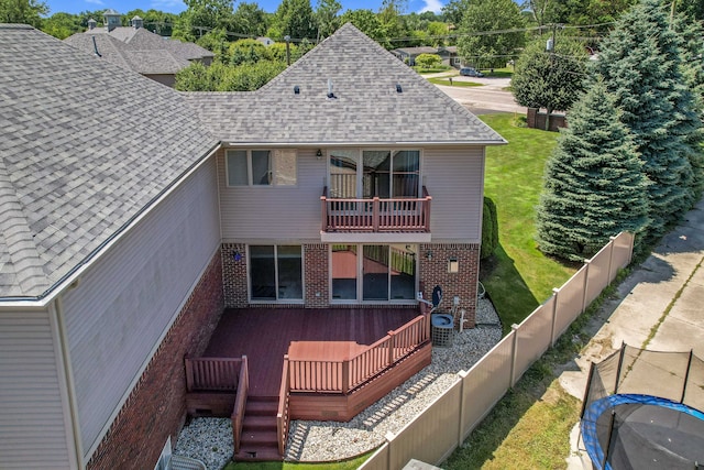 rear view of property featuring a yard, a trampoline, cooling unit, and a balcony