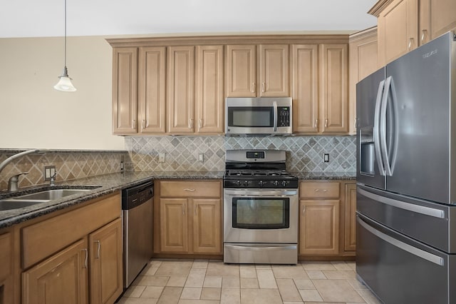 kitchen with sink, backsplash, dark stone countertops, decorative light fixtures, and appliances with stainless steel finishes