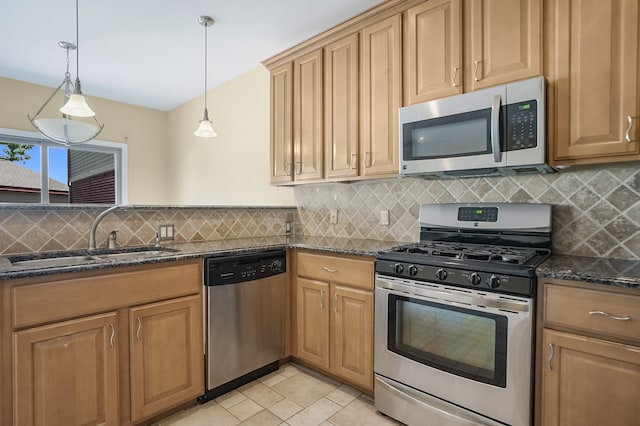 kitchen featuring decorative light fixtures, sink, stainless steel appliances, and dark stone counters