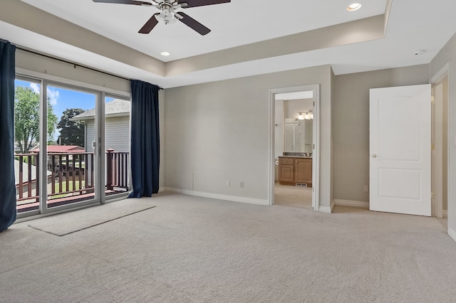 unfurnished room featuring a raised ceiling, light carpet, and ceiling fan