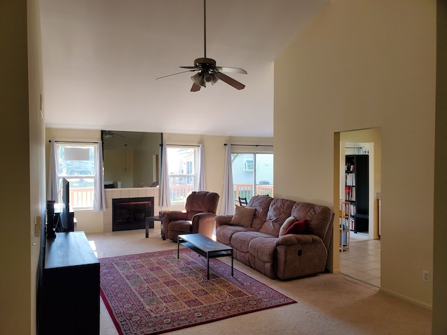 living room with a tile fireplace, ceiling fan, high vaulted ceiling, and light carpet