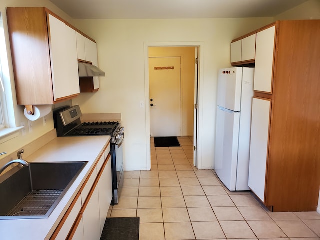 kitchen featuring stainless steel gas range oven, sink, light tile patterned floors, white refrigerator, and white cabinets