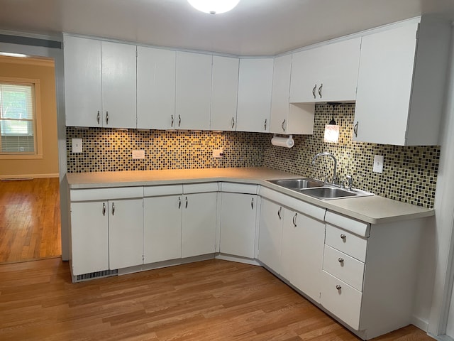 kitchen with backsplash, sink, white cabinets, and light hardwood / wood-style flooring