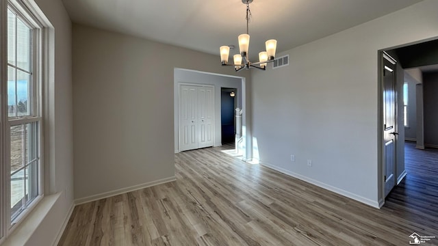 unfurnished room featuring plenty of natural light, an inviting chandelier, and light hardwood / wood-style floors