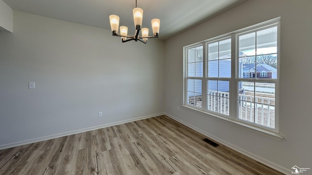 spare room featuring a healthy amount of sunlight, a chandelier, and light wood-type flooring