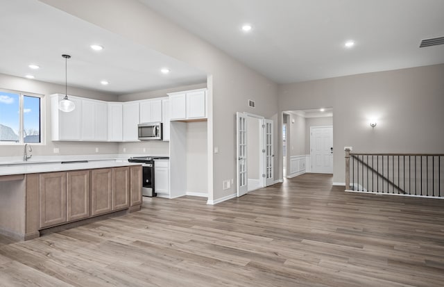 kitchen with appliances with stainless steel finishes, pendant lighting, white cabinetry, sink, and light hardwood / wood-style floors