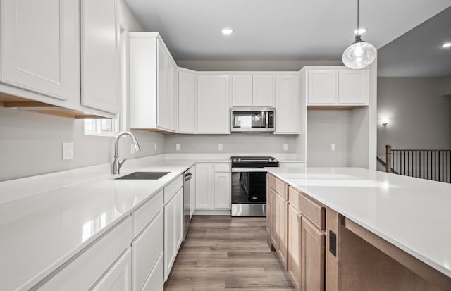 kitchen featuring wood-type flooring, sink, white cabinets, hanging light fixtures, and stainless steel appliances