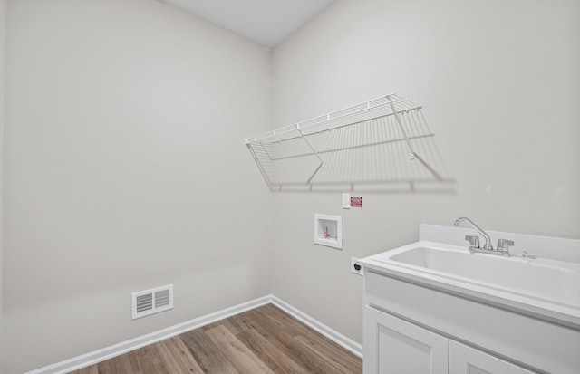 washroom with wood-type flooring, sink, cabinets, hookup for a washing machine, and hookup for an electric dryer