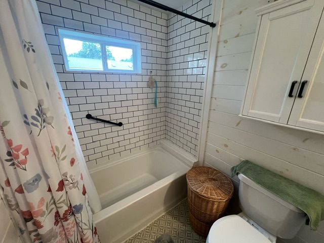 bathroom with toilet, shower / bathtub combination with curtain, and wooden walls