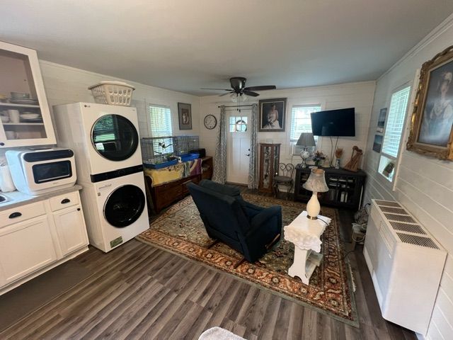 living room with stacked washing maching and dryer, dark hardwood / wood-style floors, ornamental molding, and ceiling fan