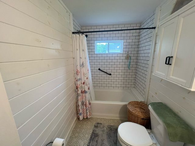 bathroom featuring toilet and shower / bathtub combination with curtain