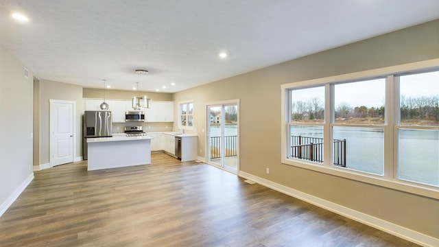 kitchen with a kitchen island, wood finished floors, white cabinetry, stainless steel appliances, and baseboards