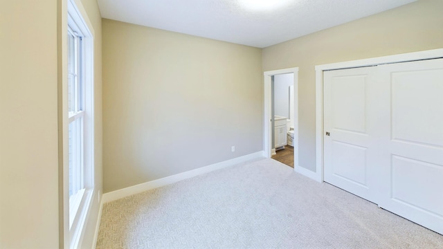 unfurnished bedroom with a closet, baseboards, connected bathroom, and carpet flooring