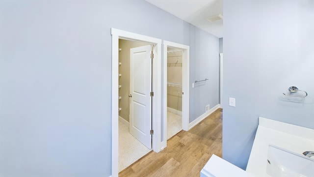 bathroom with a walk in closet, baseboards, and wood finished floors