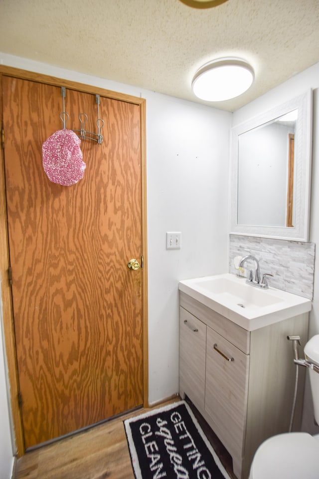 bathroom featuring vanity, backsplash, toilet, a textured ceiling, and wood-type flooring