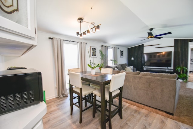 dining area featuring ceiling fan with notable chandelier, light hardwood / wood-style floors, and vaulted ceiling