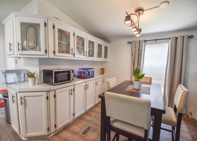 kitchen with hanging light fixtures, crown molding, light hardwood / wood-style floors, vaulted ceiling, and white cabinets