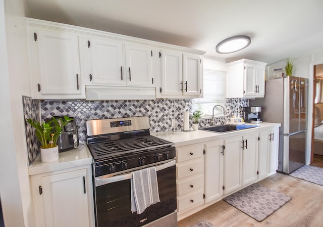 kitchen featuring sink, light hardwood / wood-style flooring, decorative backsplash, white cabinets, and appliances with stainless steel finishes