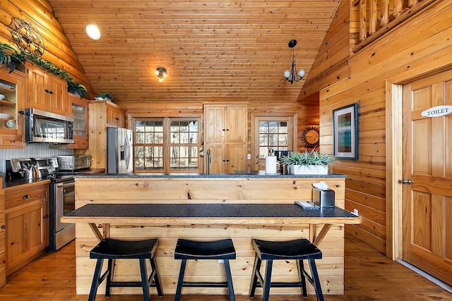 kitchen with a breakfast bar area, wood walls, stainless steel appliances, and light hardwood / wood-style floors