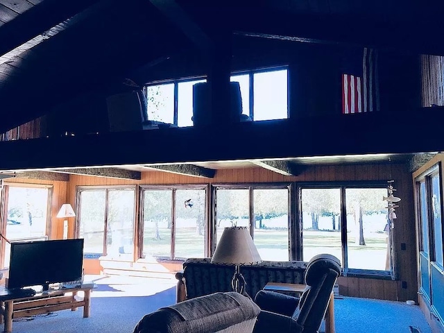 carpeted living room with vaulted ceiling with beams, a wealth of natural light, and wooden walls