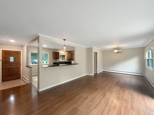 unfurnished living room featuring baseboard heating, ornamental molding, a notable chandelier, and light wood-type flooring