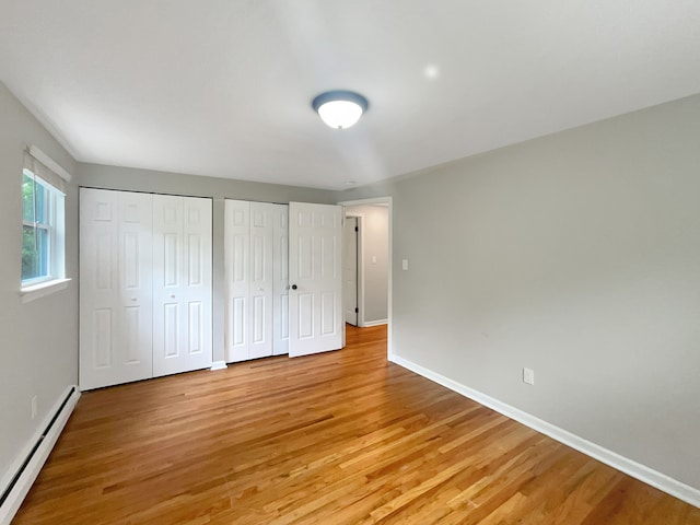 unfurnished bedroom featuring baseboard heating, multiple closets, and light wood-type flooring