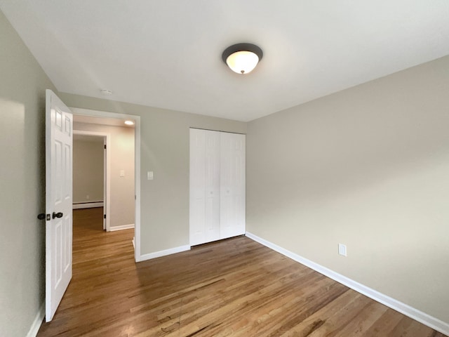 unfurnished bedroom with hardwood / wood-style flooring, a baseboard heating unit, and a closet