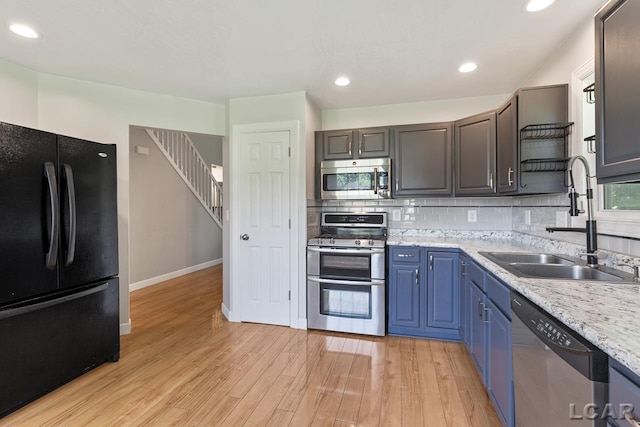 kitchen featuring backsplash, stainless steel appliances, blue cabinets, sink, and light hardwood / wood-style floors