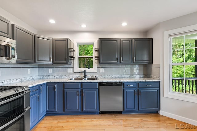 kitchen featuring backsplash, blue cabinets, light wood-type flooring, and appliances with stainless steel finishes