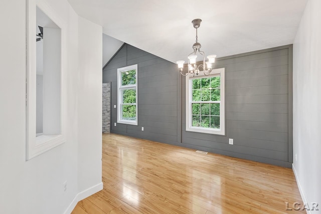 empty room with ceiling fan with notable chandelier, light hardwood / wood-style floors, a wealth of natural light, and vaulted ceiling