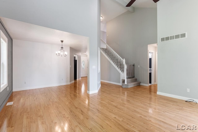 unfurnished living room featuring beam ceiling, high vaulted ceiling, light hardwood / wood-style floors, and ceiling fan with notable chandelier