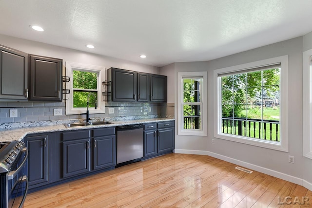 kitchen with sink, decorative backsplash, light stone countertops, light wood-type flooring, and stainless steel appliances