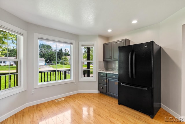 kitchen with gray cabinetry, black fridge, and light hardwood / wood-style flooring