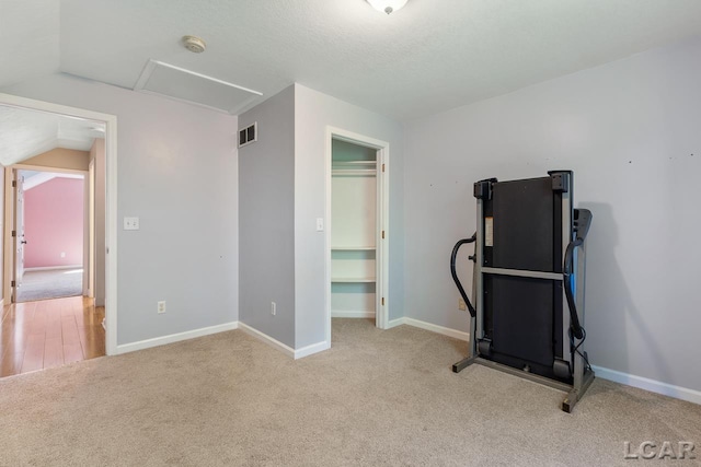 exercise room with light colored carpet, a textured ceiling, and vaulted ceiling