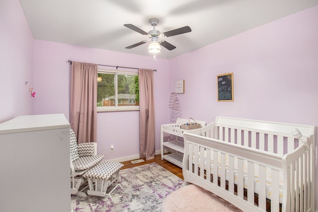 bedroom featuring ceiling fan, light hardwood / wood-style flooring, and a crib