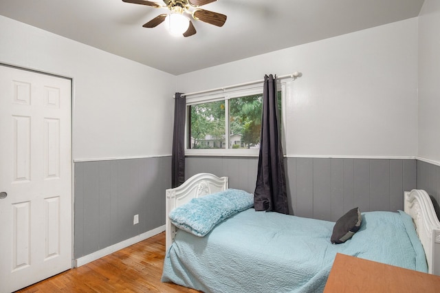 bedroom featuring ceiling fan, light wood-type flooring, and wooden walls