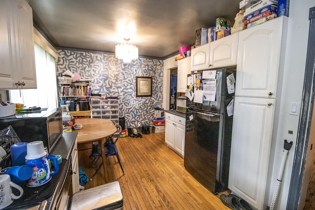 kitchen featuring crown molding, a chandelier, light hardwood / wood-style floors, black refrigerator, and white cabinets