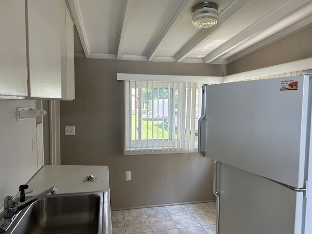 kitchen featuring wooden walls, sink, beamed ceiling, white fridge, and light tile patterned flooring